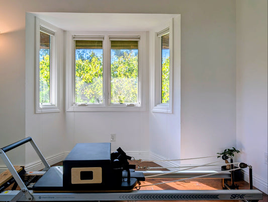Pilates reformer machine in a room with large windows and a lamp.